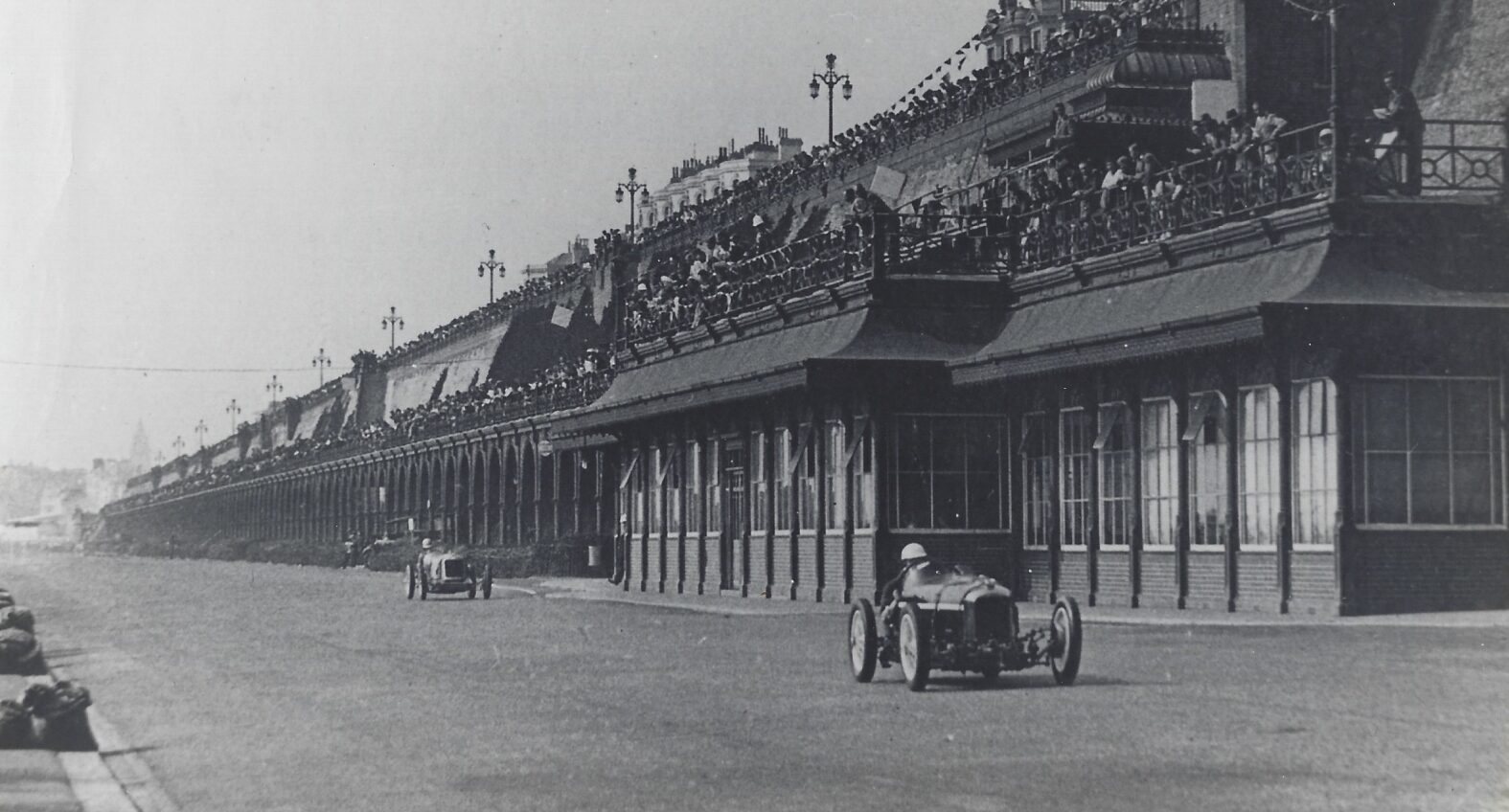 Vintage photo of Amilcar C6 Brooklands Voiturette racing past stand